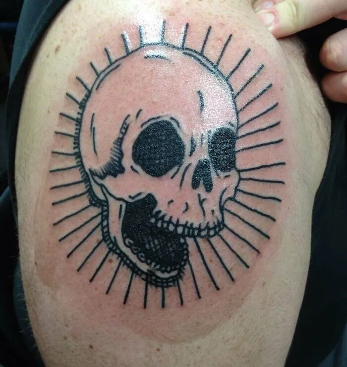 Minimalist tattoo of a skull with radiating lines, inked on upper arm. Aesthetically pleasing design.