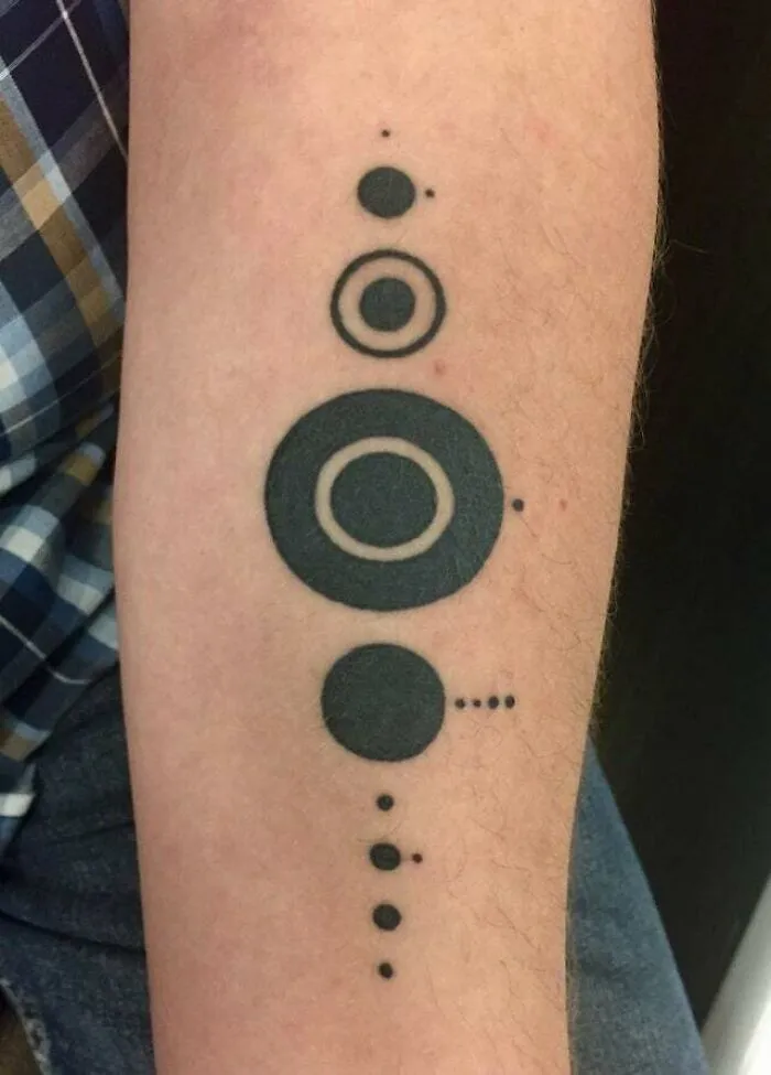 Minimalist tattoo of black circles and dots arranged in a vertical line on an arm.