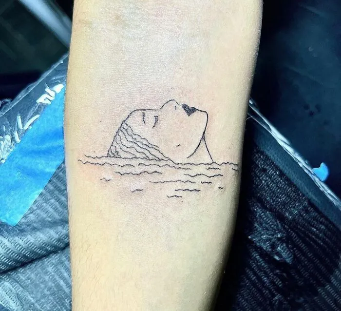 Minimalist tattoo of a face emerging from water, showcasing aesthetically pleasing design on forearm.