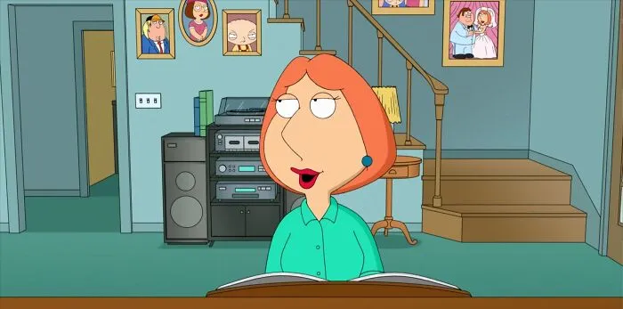 Female cartoon character with red hair sitting in a living room with framed photos on the wall.