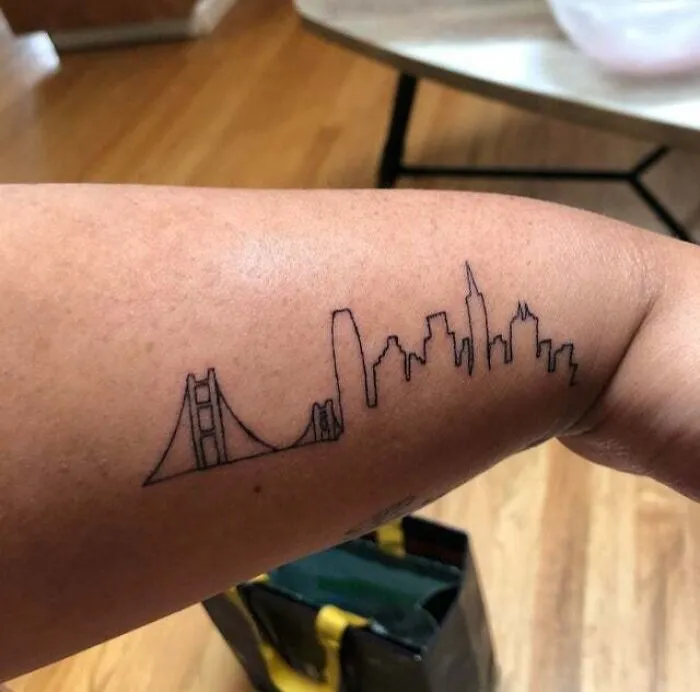 Minimalist tattoo of a city skyline and bridge on a forearm, showcasing simple and aesthetically pleasing design.