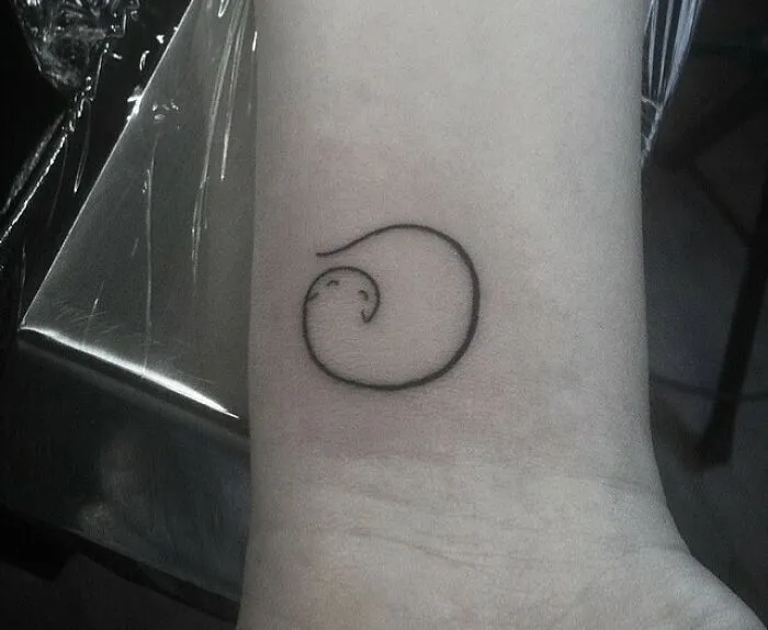 Minimal tattoo design of a small, abstract swirl on a wrist.