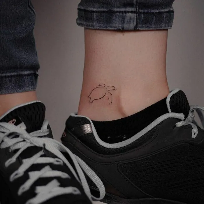 Minimal tattoo design of a simple turtle on an ankle, next to black sneakers and blue jeans.