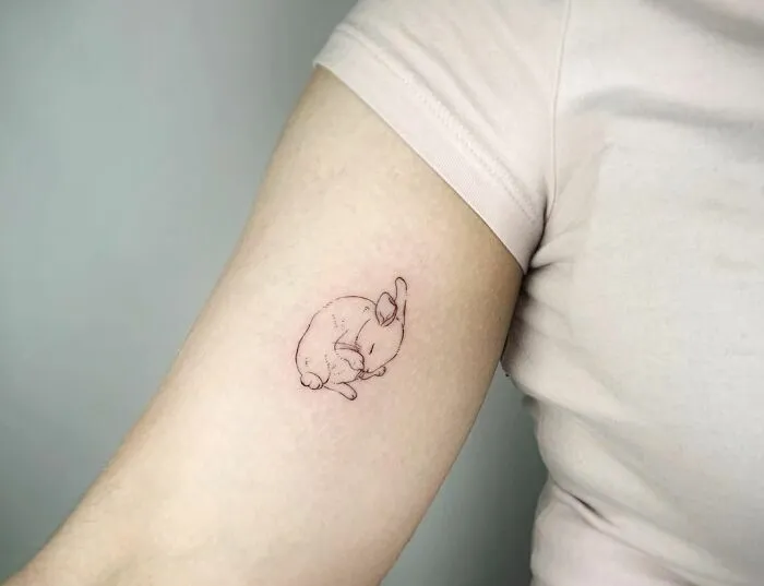 Minimal tattoo of a sleeping rabbit on an arm, showcasing delicate line work in understated tattoo design.