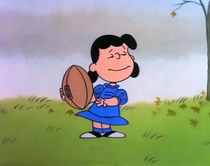 Female cartoon character holding a football, standing confidently on a grassy field.