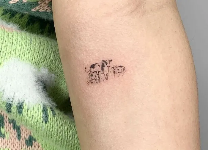 Minimal tattoo design on arm featuring a small cow family, showcasing intricate and detailed ink work.