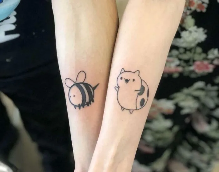 Two forearms with minimalist tattoos, one a bumblebee and the other a playful cat design, showcasing minimalist tattoo art.