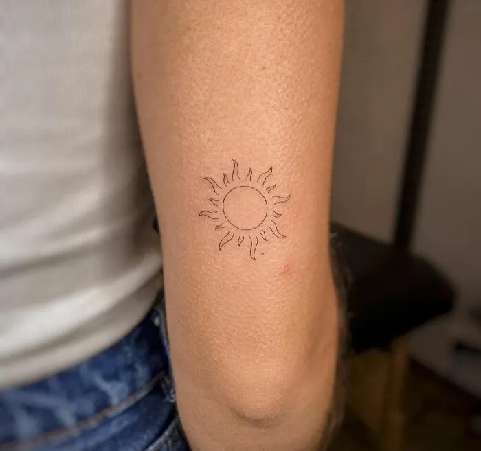Minimalist tattoo of a small sun on an arm, showcasing simplicity and elegance in design.