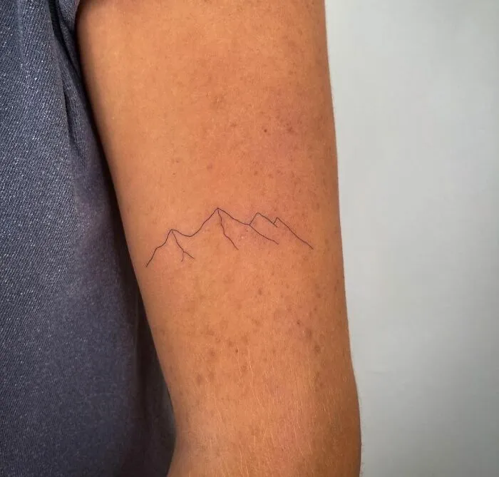 Minimalist tattoo of mountain outline on a person's arm, showcasing a simple and aesthetically pleasing design.