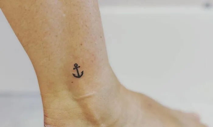 Minimalist tattoo of a small anchor on an ankle, showcasing aesthetically pleasing design.