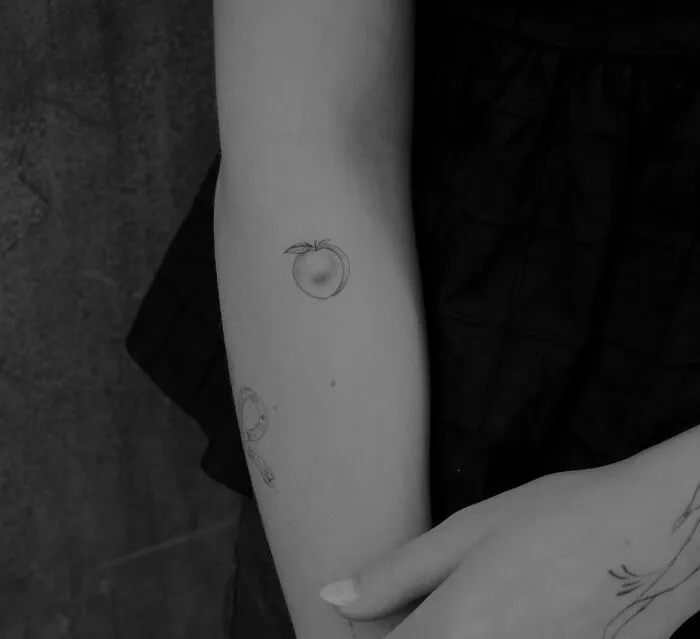 Minimalist tattoo of a small peach on a person's forearm, emphasizing a simple and aesthetically pleasing design.