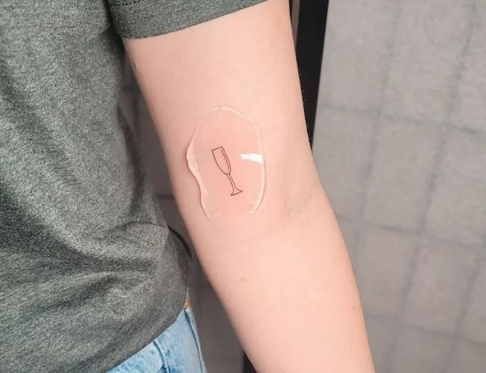 Minimalist tattoo of a champagne glass on a person's arm.