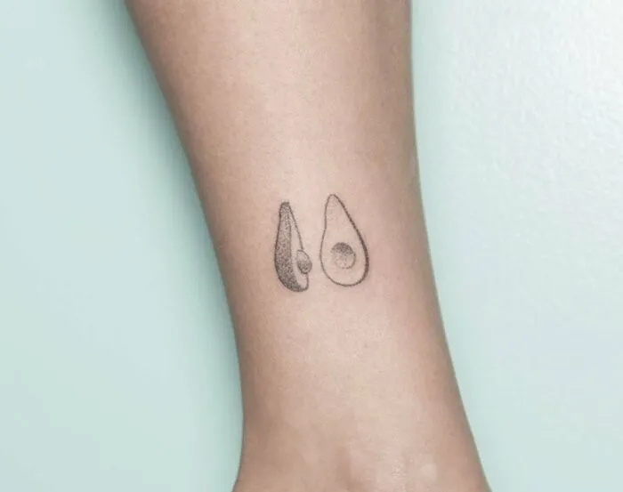 Minimalist tattoo of an avocado, simple and aesthetically pleasing on forearm.