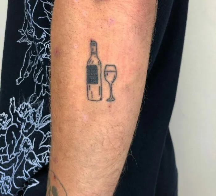 Minimalist tattoo of a wine bottle and glass on an arm.