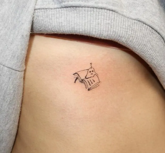 Minimalist tattoo of a small robot reading a book on skin. Aesthetically pleasing design.