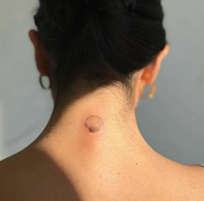 Minimalist tattoo of a small shell on the back of a person's neck, showcasing simple and aesthetically pleasing design.
