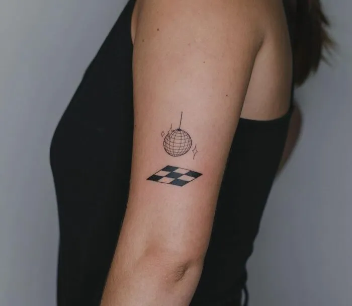 Minimalist tattoo of a disco ball and chessboard pattern on upper arm, simple and aesthetically pleasing design.