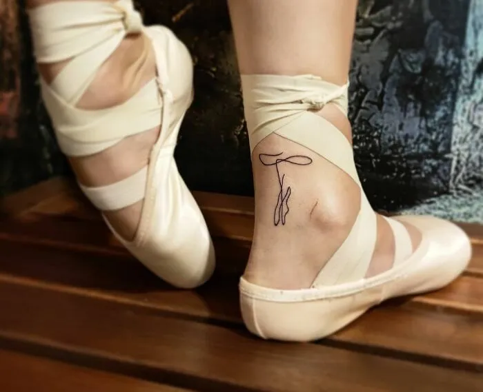 Minimalist tattoo on a dancer's ankle in pointe shoes, featuring a delicate, abstract design.