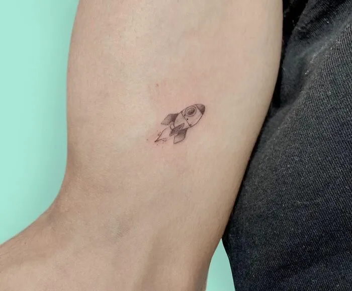 Minimalist tattoo of a small rocket on an arm, showing aesthetically pleasing design.