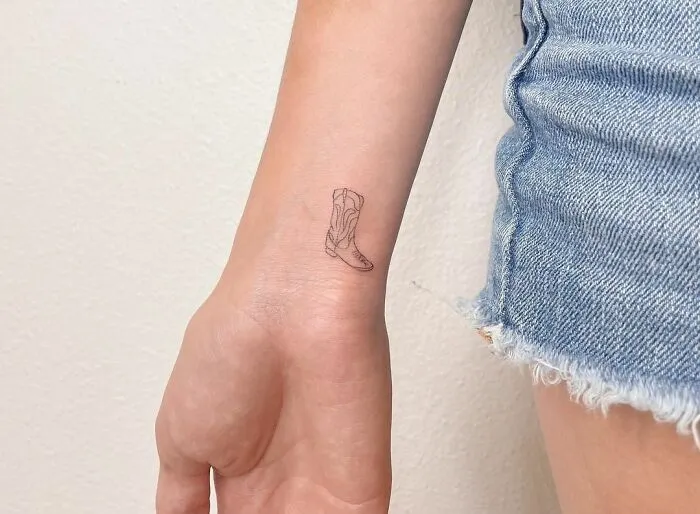 Minimalist tattoo of a cowboy boot on a person's forearm, showcasing delicate line art for an aesthetically pleasing look.