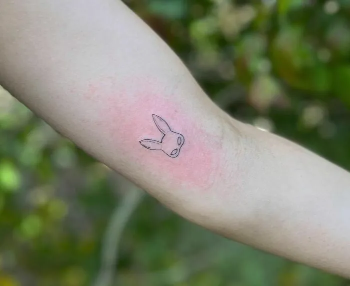 Minimalist tattoo of a small bunny head on an arm, featuring simple black linework.
