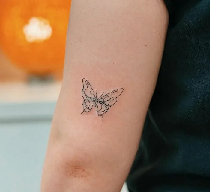 Minimalist butterfly tattoo on arm, showcasing aesthetically pleasing line art design.