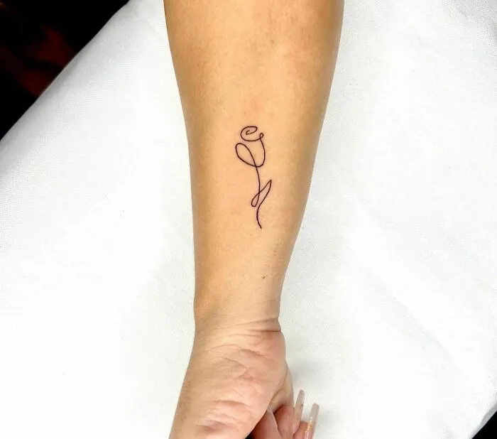 Minimalist tattoo of a delicate rose outline on a person's forearm.