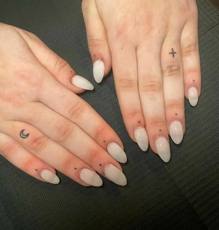 Minimalist tattoos on fingers, featuring small symbols and designs, surrounded by simple, natural nails.