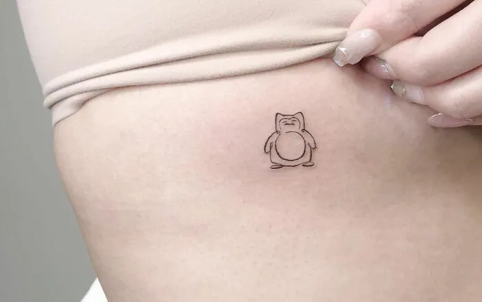 Minimal tattoo design of a cartoon character on a person's side, with a hand gently touching the skin.