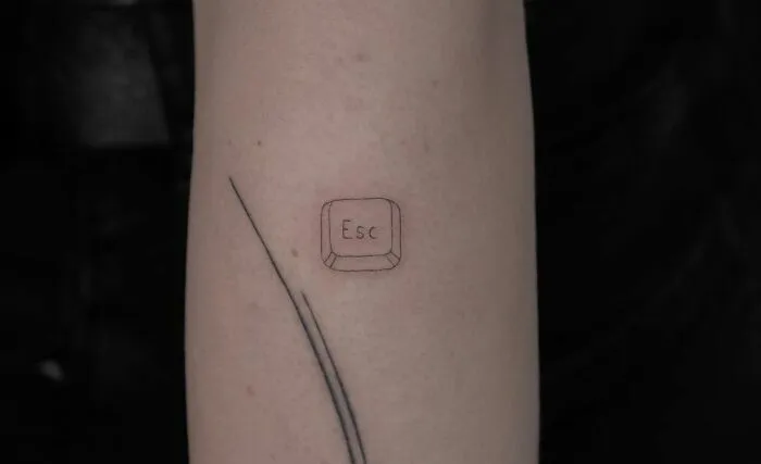 Minimal tattoo featuring an "Esc" key on a person's arm with a simple line design in a minimalist style.