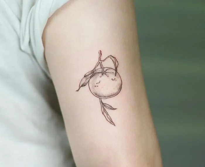 Minimal tattoo design of a delicate orange with leaves on an arm.