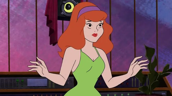 Female cartoon character with red hair in a green dress, showcasing fame and strength in a colorful room.