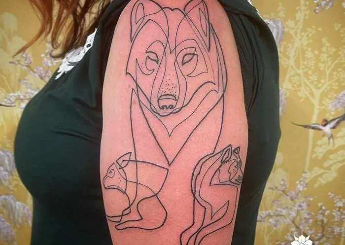 Fine-line single-line tattoo of abstract animals on an arm.