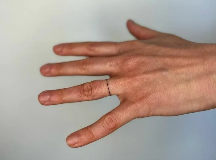 Close-up of a hand with a minimal single-line tattoo ring on the finger, showcasing fine-line perfection.