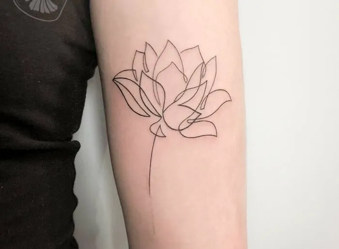 Single-line tattoo of a lotus flower on an arm, showcasing fine-line artistry.