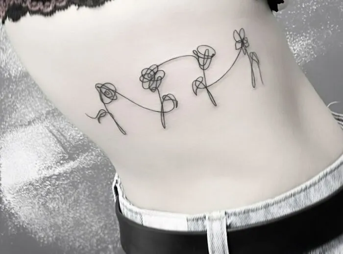 Fine-line tattoo of single-line flowers on a person's side.