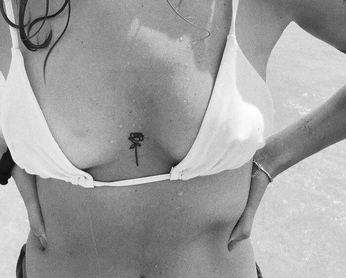 A fine-line single rose tattoo on a woman's chest in a bikini.