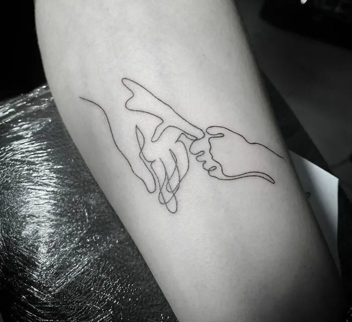 Fine-line single-line tattoo of two hands touching, on an arm.