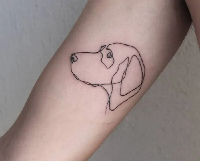 Single-line tattoo of a dog's face in fine-line style on an arm.