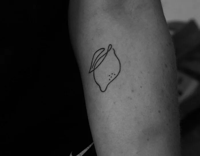 Fine-line perfection single-line tattoo of a lemon on an arm.