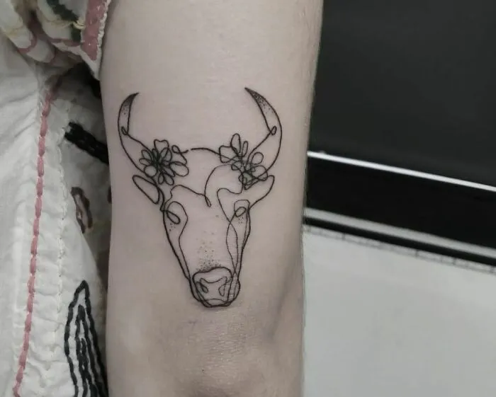 Single-line tattoo of a bull with floral details on an arm; showcases fine-line perfection.