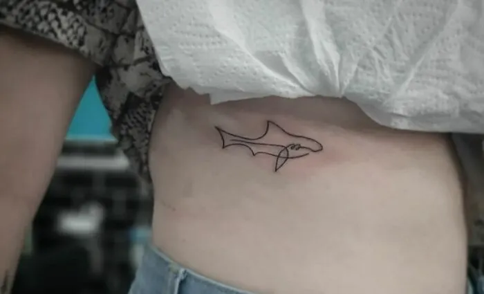 Single-line fine-line tattoo of a shark on a person's side, showcasing minimalist body art.