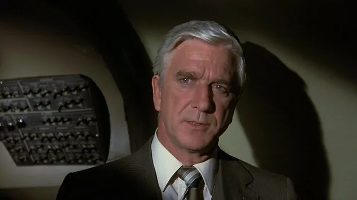 Leslie Nielsen wearing a suit in a scene from Airplane movie, featured among famous people who got married multiple times.