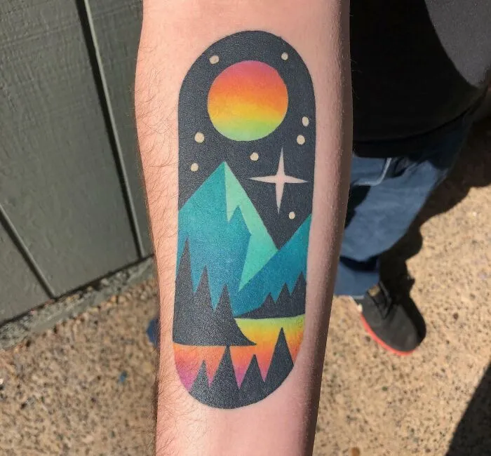 Colorful trippy tattoo of mountains and space on a forearm, featuring a psychedelic sun and starry sky design.