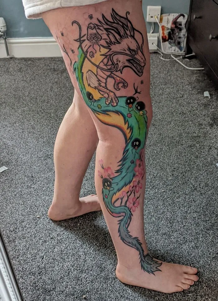 Leg displaying trippy tattoo with a vibrant dragon and fantastical elements on a gray carpeted floor.