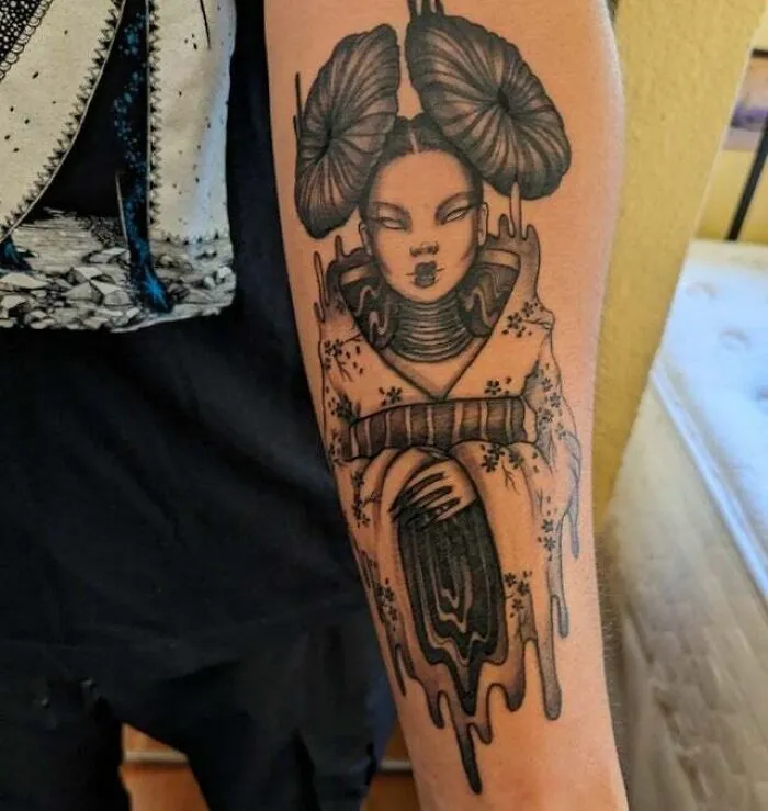 Trippy tattoo of a surreal geisha face with flowing patterns on an arm.