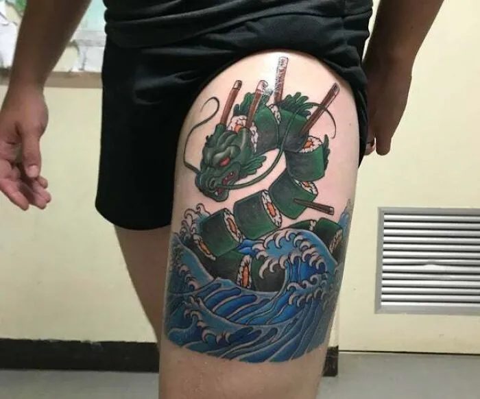 Trippy tattoo of a dragon composed of sushi rolls and chopsticks, swirled with ocean waves on a person's thigh.