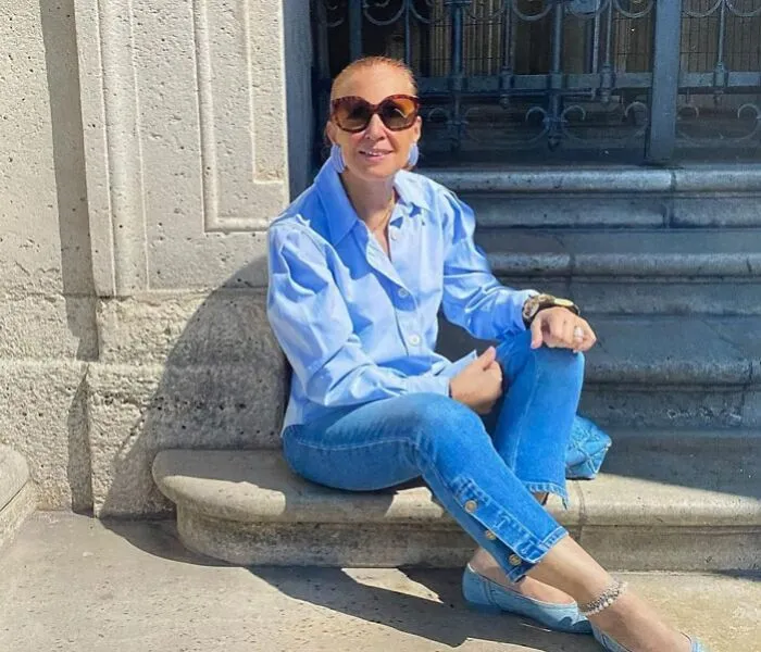 Danielle Steel wearing blue shirt and jeans, sitting outdoors in sunlight, related to famous people married multiple times.