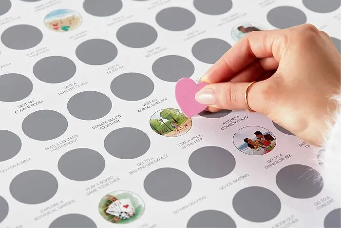 Hand holding a pink heart-shaped piece on a love-themed scratch-off adventure calendar, ideal Valentine's Day gift.