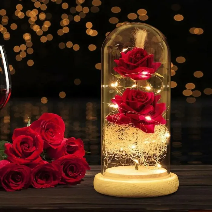 Valentine's Day gift display with red roses in a glass dome, surrounded by warm fairy lights and rose bouquet.